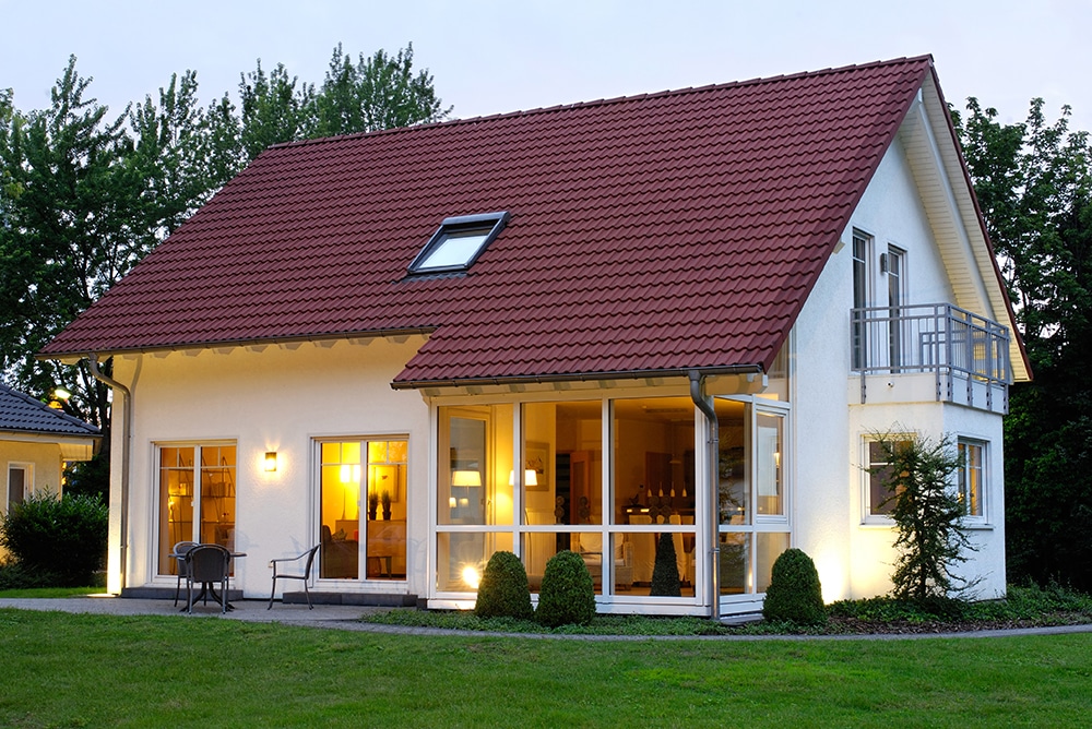 Cozy two-story house with red roof and illuminated windows at dusk.