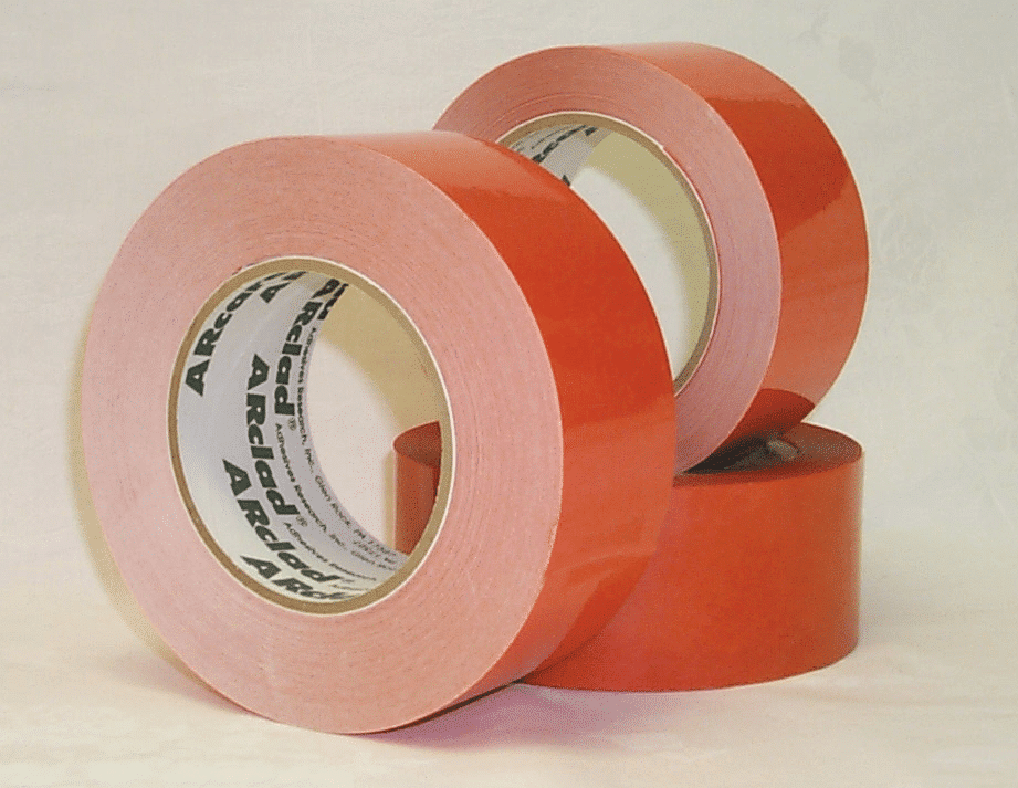 Three rolls of red adhesive tape from Adhesives Research are stacked on a white surface, with labels visible inside the rolls.